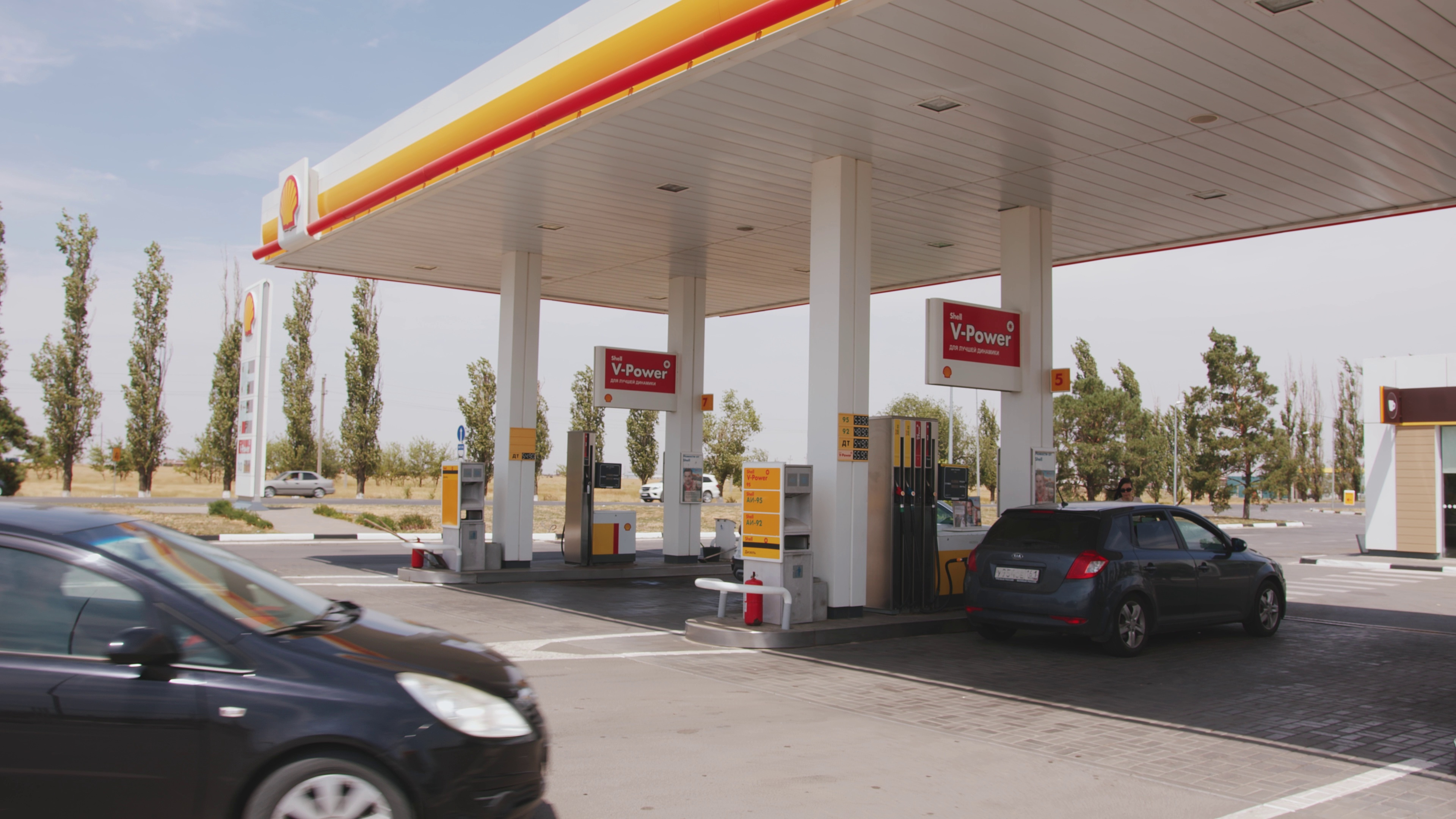 two cars pulling into a Shell gas station near a highway