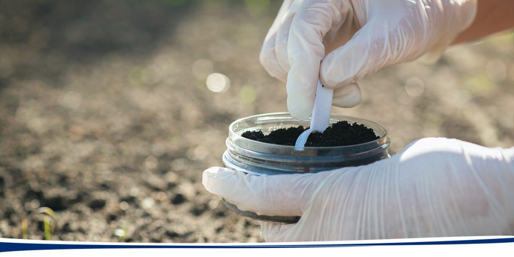 hands wearing white gloves taking a soil sample